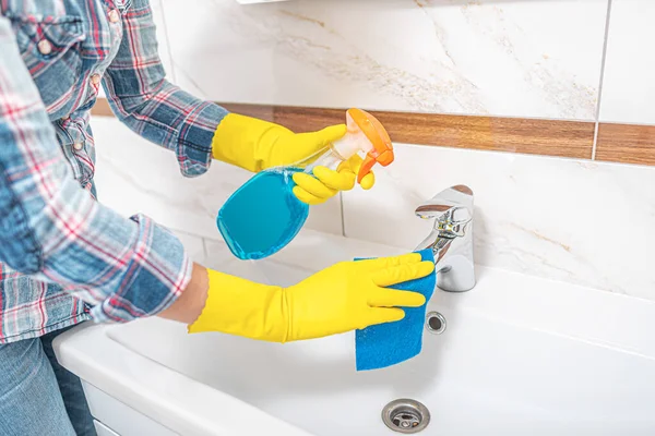 Pulizia in bagno. Una donna pulisce il lavandino e il rubinetto del lavabo . — Foto Stock