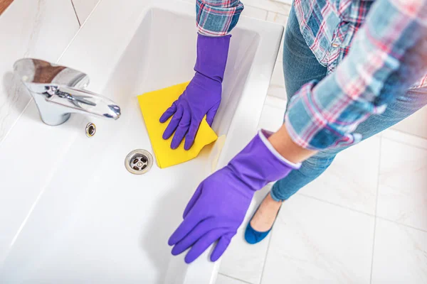 Limpeza na casa de banho. Uma mulher limpa a pia e a torneira do lavatório . — Fotografia de Stock