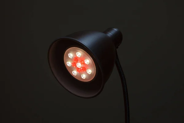 Close-up of a LED lamp white and red color. Round table lamp with a new technology lamp on black background.
