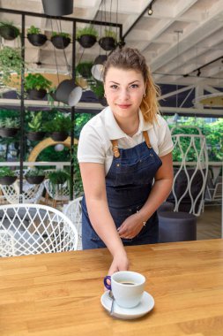 Bir mutlu oldukça kadın garson kahve Cafe ile ayakta ve kameraya bakarak önlük.
