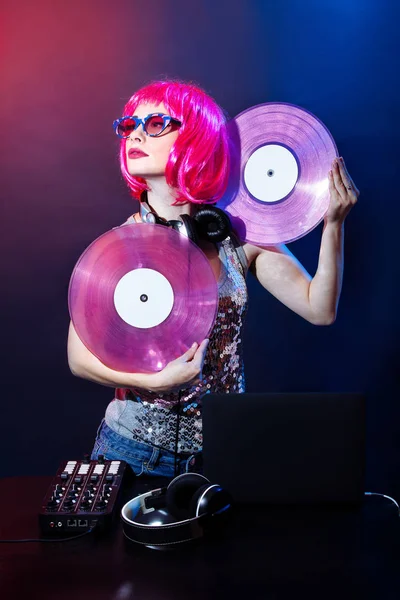 Pembe saç ve kırmızı ve mavi arka plan üzerinde vintage gözlük ile genç bir kadın portresi. DJ ve kadın ile headphne pembe vinyls müzik disko çalıyor. Glamour parti yaz Club ekipman.