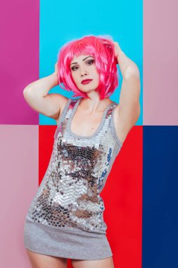 Çok renkli grafik arka plan gümüş elbiseyi giymiş pembe saçlı güzel kız. Mutlu bir kadın duygusal olarak ellerini dokunur baş.