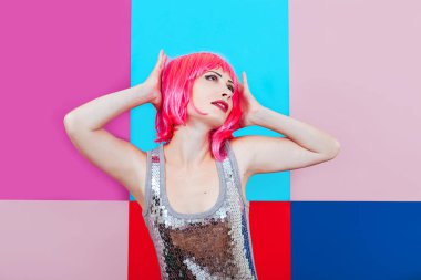 Çok renkli grafik arka plan gümüş elbiseyi giymiş pembe saçlı güzel kız. Mutlu bir kadın duygusal olarak ellerini dokunur baş.