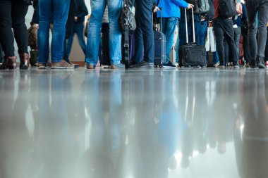 Birçok kişi havaalanında check-in için sırada bekliyor. Bagaj grubu alt kısmında yerde yansıtılır.