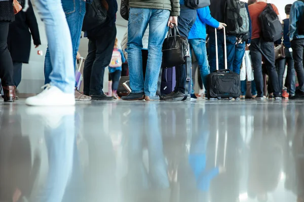 Birçok kişi havaalanında check-in için sırada bekliyor. Bagaj grubu alt kısmında yerde yansıtılır.