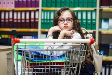Küçük bir kız okul için ileti örneği alıyor. Bir el arabası ile bir süpermarkette Gözlüklü kız öğrenci. Geri okul kavramı.