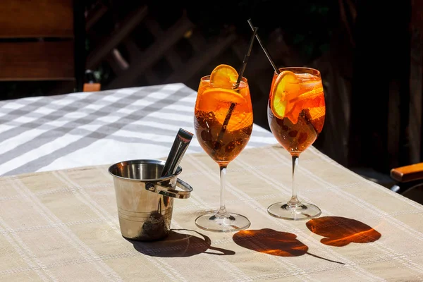 Aperol 在木桌上的玻璃杯里喷出鸡尾酒 两杯鸡尾酒和一个冰桶在桌子上的阴影 — 图库照片