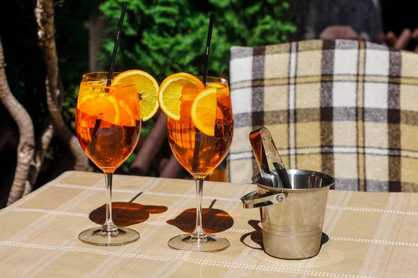 Aperol 在木桌上的玻璃上喷鸡尾酒 叶子的背景 两杯鸡尾酒和桌上的冰桶 — 图库照片