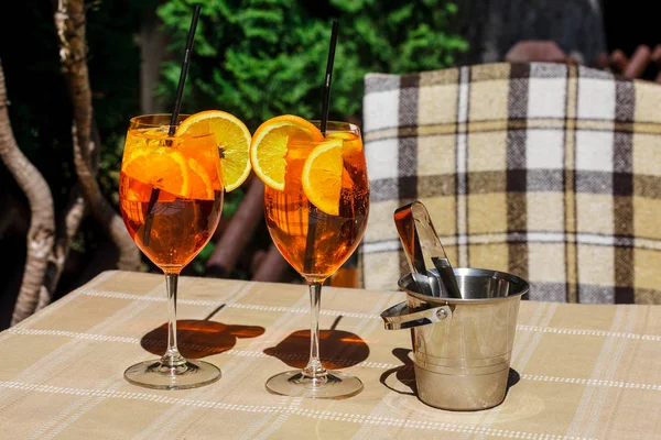 Aperol スプリッツの木製のテーブルと葉の背景にガラスのカクテル カクテルとテーブルの上の氷のバケツ — ストック写真