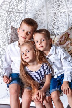 İki kardeş ve birlikte kameraya bakarak mavi gözlü bir kız. Birlikte oturan mutlu gülümseyen çocuklar Grup.