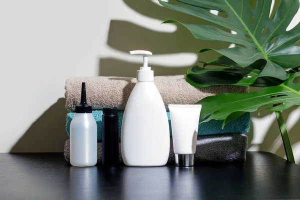 Cosmetics in white tubes and bath products on a black table with tropical leaves. Means of hygiene and washcloth for women's health, SPA concept.