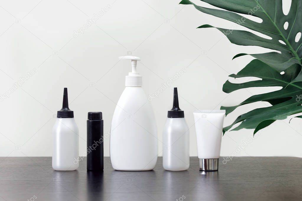 Cosmetics in white tubes and bath products on a black table with tropical leaves. Means of hygiene for women's health, SPA concept.