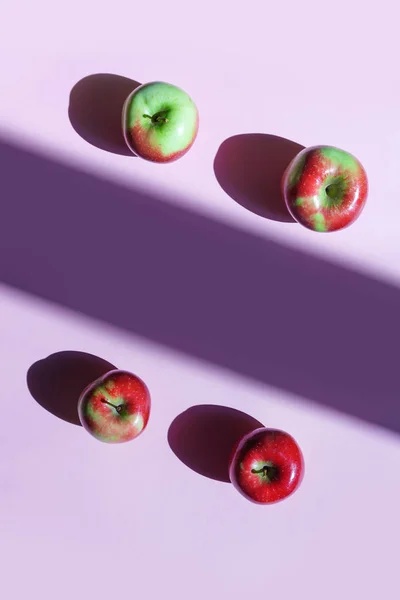 Ripe yellow and red apples on a lilac background, light and shadow concept.