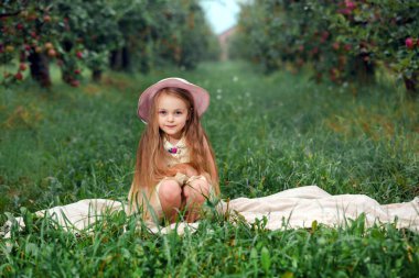 Küçük kız bir beyaz elbise ve şapka bir elma bahçesinde.