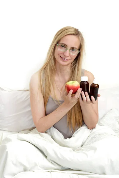 プラス女性ベッドの上に座ってリンゴを保持しているし 彼女の手の薬を飲んでいます 更年期の間に本物のポートレート幸せな女 — ストック写真
