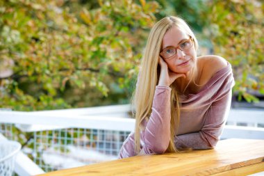 Orta yaş kadın, Sarışın, pembe elbise ve gözlük standları sonbahar yaprakları çerçevede giyinmiş 50 artı. Bir kadının menopoz dönemindeki güzelliği.