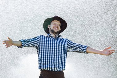 Şapkalı çiftçi yağmur keyif alıyor. Yaz aylarında yağmur altında ıslak genç adam.