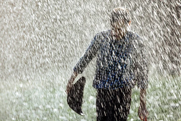 The farmer in the hat is enjoying the rain. Young man getting wet under the rain in summer.