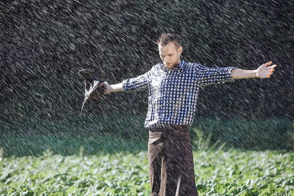 The farmer in the hat is enjoying the rain. Young man getting wet under the rain in summer.