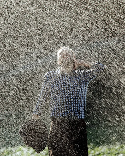 The farmer in the hat is enjoying the rain. Young man getting wet under the rain in summer.