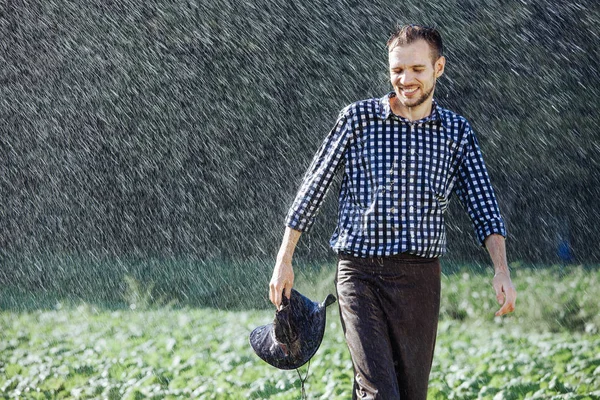 The farmer in the hat is enjoying the rain. Young man getting wet under the rain in summer.