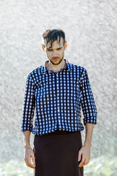 Portrait of a strong, drenched man in the rain. Young man getting wet under the rain in summer.