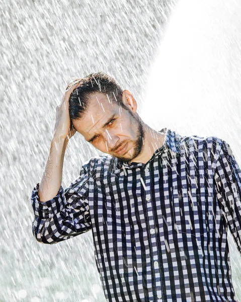 Portrait of a strong, drenched man in the rain. Young man getting wet under the rain in summer.