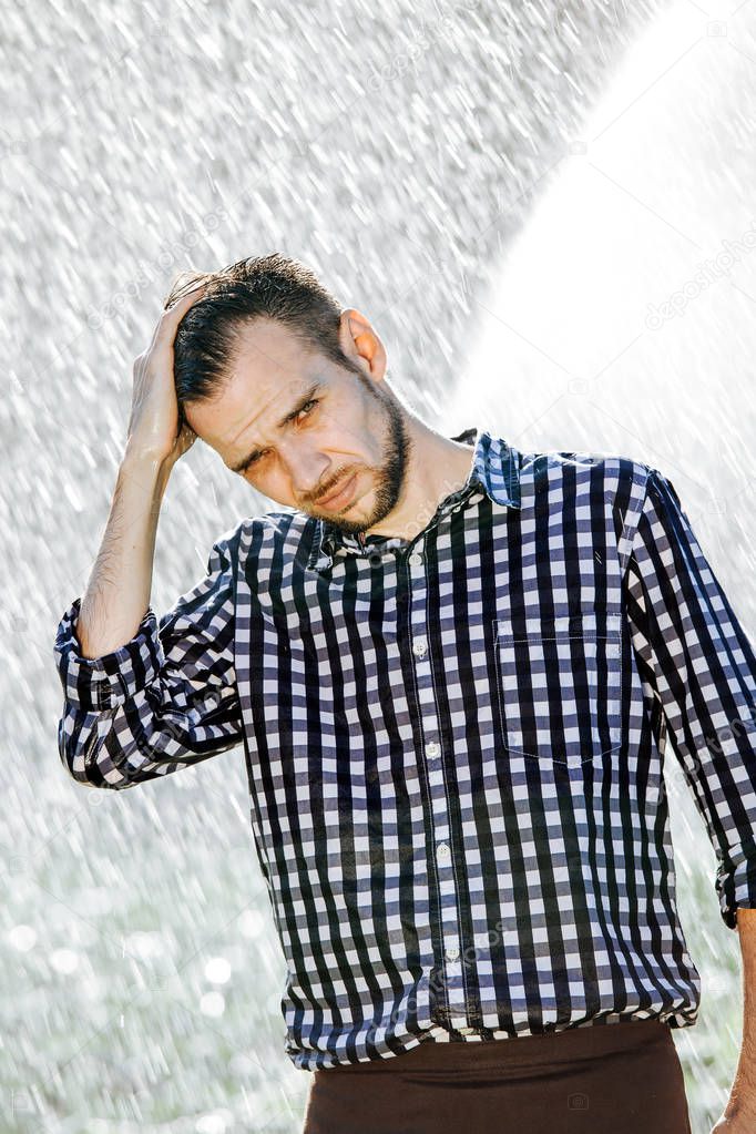 Portrait of a strong, drenched man in the rain. Young man getting wet under the rain in summer.