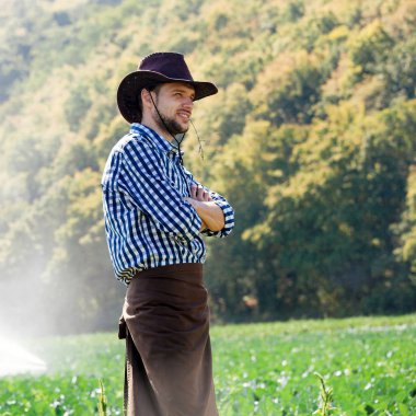 Çiftçi sahada sulama veya yağmurlama sistemi arka plan üzerinde duruyor. Genç bir ziraat mühendisi bir plantasyonda olduğunu ve hasat kalite denetimleri.