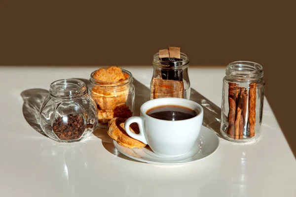 ミルクティーのカップと砂糖と透明な瓶のスパイスの棒 一杯のコーヒーと白い背景の上のガラス瓶にシナモン — ストック写真