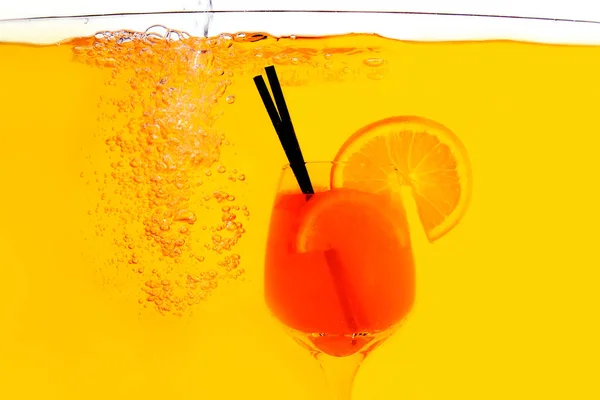 Aperol スプリッツ カクテル オレンジ色の背景上に水のガラスに内側 オレンジ ジュースは赤と白のアクリル絵の具を水の下で ロイヤリティフリーのストック画像