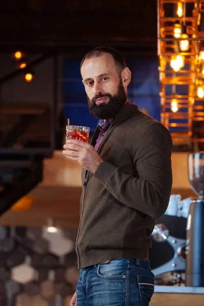 Bearded man in a cafe drinking mulled wine. Businessman in the office in a loft style holds a glass with a red hot drink.