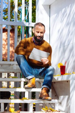 Sakallı adam mulled şarap içme bir kafede. İşadamı ofiste çalışıyor, bir cam bir kırmızı sıcak içecekle tutar ve tablet kullanır.