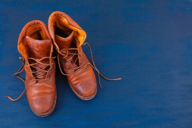 Old red dirty high shoes on blue background. Old school vintage worn boots with leather laces.