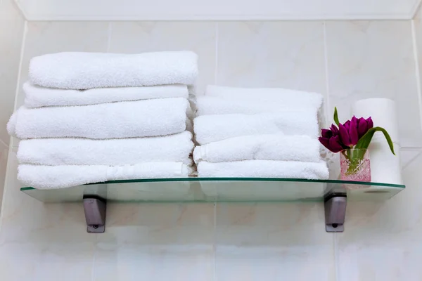 Lots of white towels in the bathroom. Clean white towel on a shelf prepared to use.