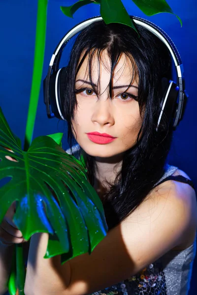 Brunette girl on tropical leaves background. DJ woman plays music disko party on the equipment in the summer club.