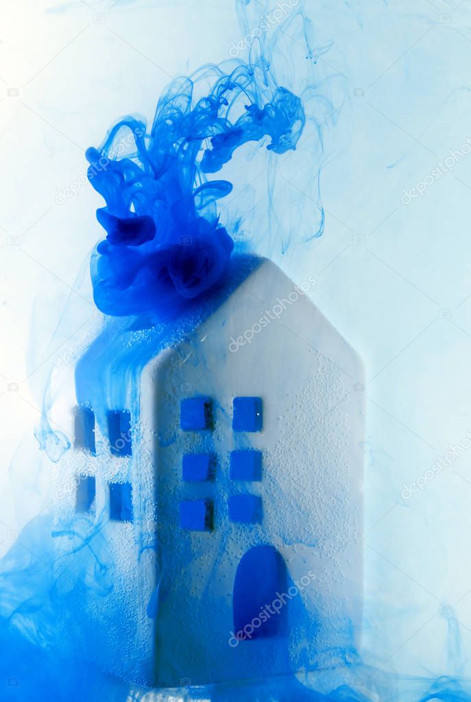 Small ceramic house under the water with blue acrylic paints. The concept of real estate, rent, sale or heating. White house from fairy tale.