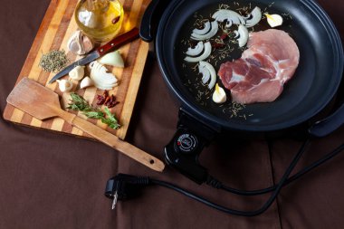 Masanın üzerinde domuz eti ile elektrikli tava. Herhangi bir yerde yemek pişirmek için bağımsız yardımcı tava.