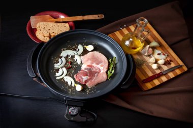 Masanın üzerinde domuz eti ile elektrikli tava. Herhangi bir yerde yemek pişirmek için bağımsız yardımcı tava.