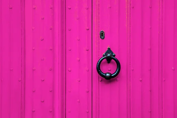 A black forged handle on the pink door. Old vintage door with iron handle.