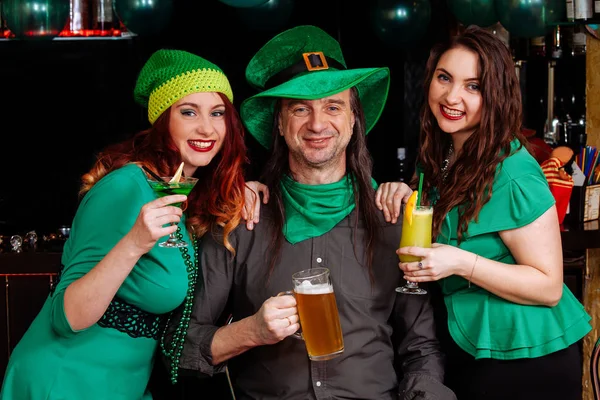 The company of young girls and one man celebrate St. Patrick\'s Day. They have fun at the bar. They are dressed in carnival headgear, green hats and clothes.