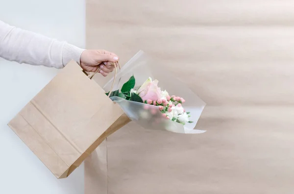 Hands of Worker of Delivery Service Packing Flowers in paper bag for Customer on the White and Craft Background.