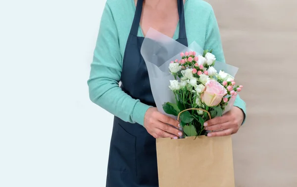 Female Worker of Delivery Service in Uniform Packing Flowers in paper bag for Customer on the White and Craft Background.