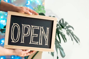 Kadının elleri metin açık bir şekilde gösterge panelini tutuyor. Önlüklü işçi, kafenin ya da pazarın açılışındaki vitrin ışıklarıyla gösteriyor.