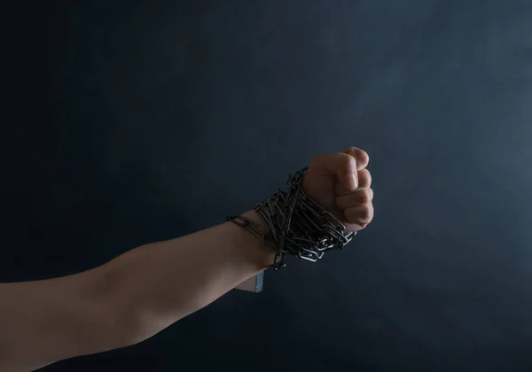 Fist of Hand are chained in chains on the black background, concept of Fight and Freedom.