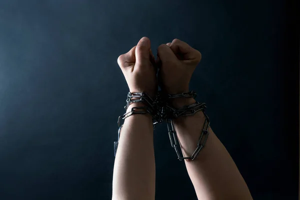 Fists of Hands are Chained in Chain on the black background, concept of Fight and Freedom.