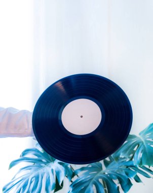 Yeşil tropikal yaprakların arka planında klasik bir plak çalar ve elinde siyah vinil plak var. Eski usul..