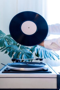 Yeşil tropikal yaprakların arka planında klasik bir plak çalar ve elinde siyah vinil plak var. Eski usul..