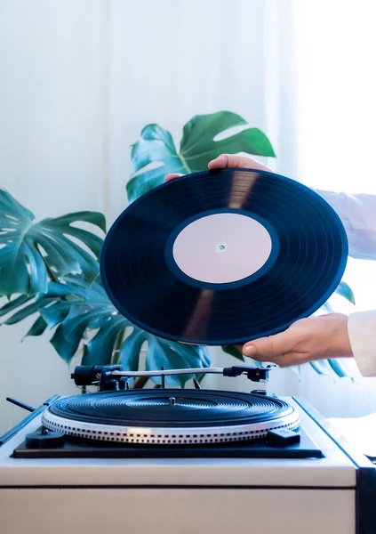 Vintage record player and hand holding black vinyl record on the green tropical leaves background. Old school style.