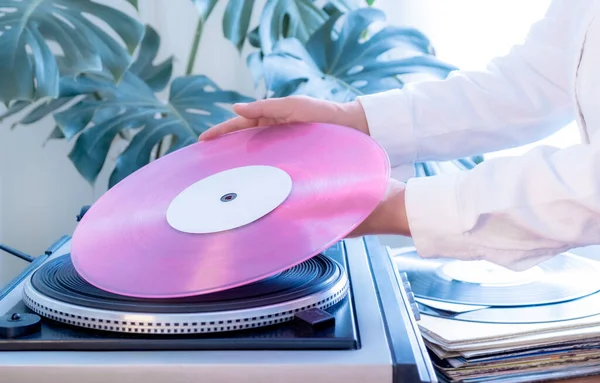 Vintage record player and hand holding pink vinyl record on the green tropical leaves background. Old school style.